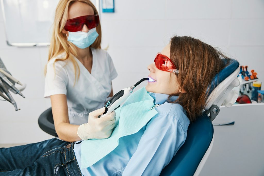 Female dentist setting sealants on teeth with LED curing lights